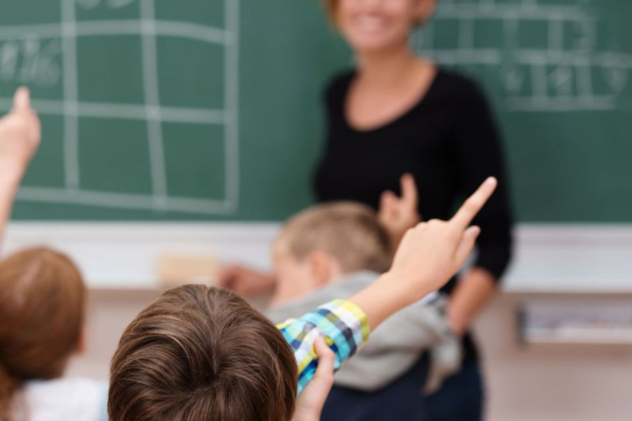 Lehrerin steht an der Tafel und Kinder melden sich.