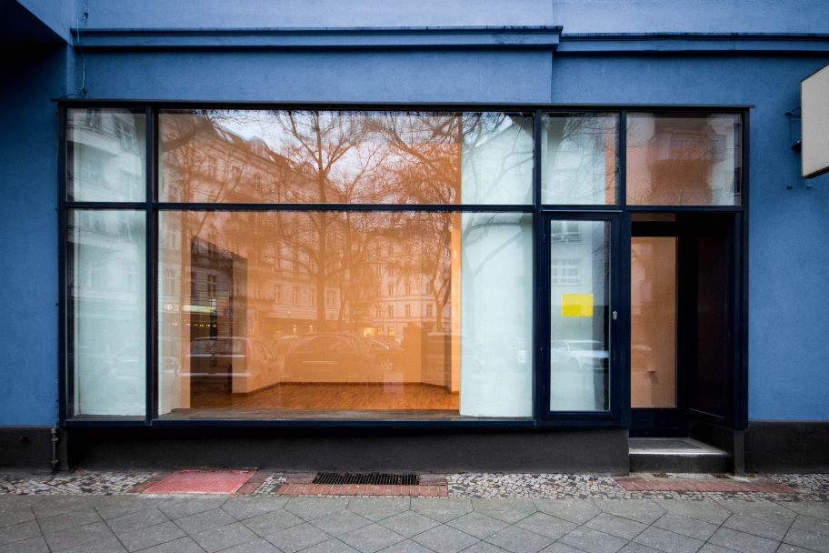 Fensterfront eines leer stehenden Geschäfts mit schwarzen Fensterrahmen, einer blauen Fassade und innen mit Dielenparkett