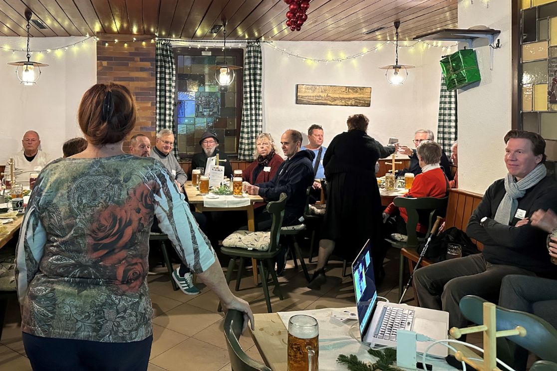 Menschen in einem Wirtshaus, im Vordergrund eine Rednerin und ein Notebook