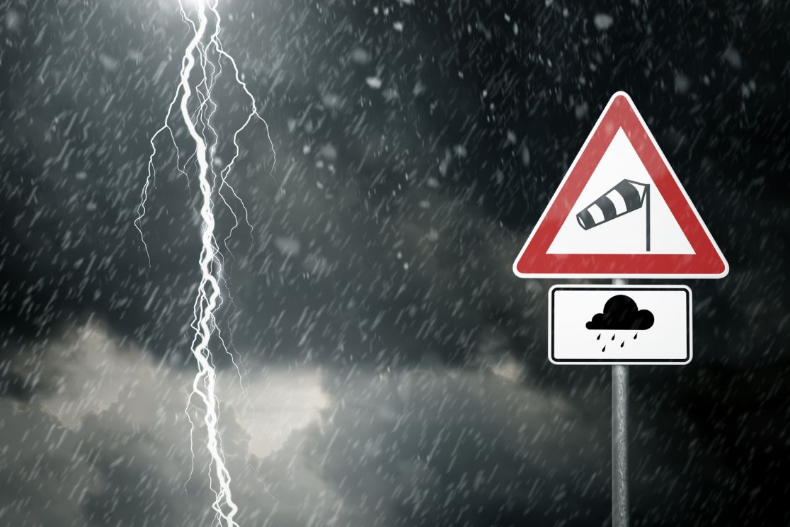 Blitz vor dunklem Himmel und Schild mit Warnung vor Sturm und Regen