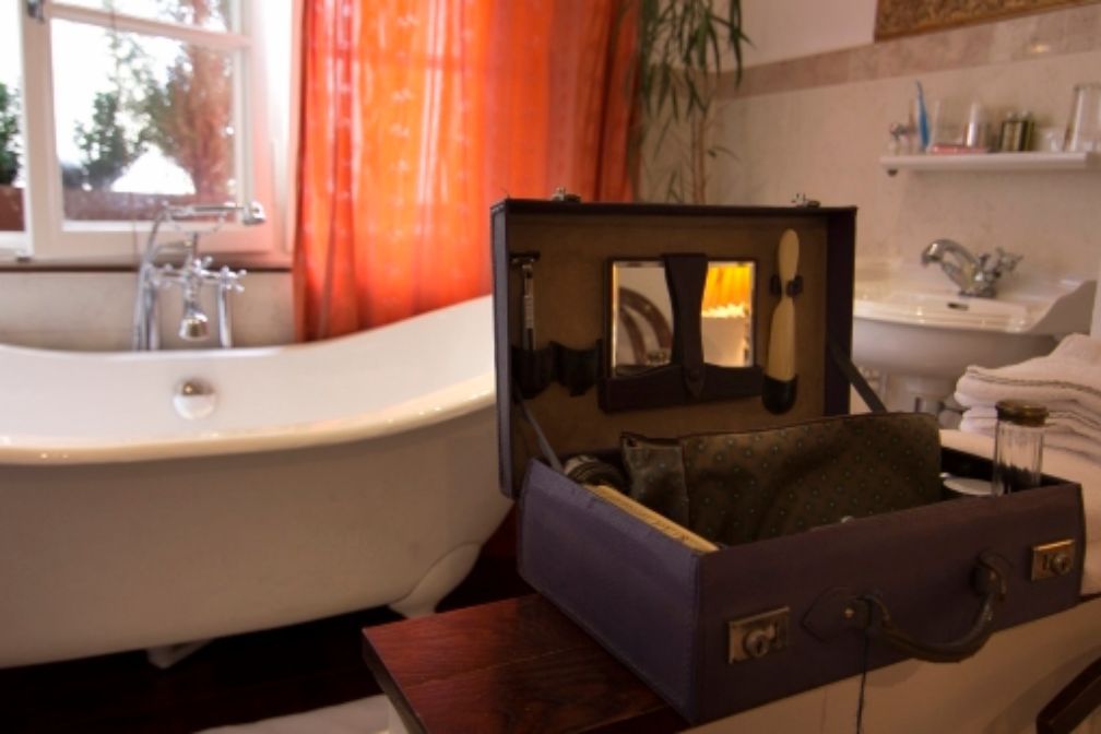 Ein geöffneter Koffer in einem Hotelzimmer, in dem im Hintergrund eine altmodisch anmutende Badewanne steht.