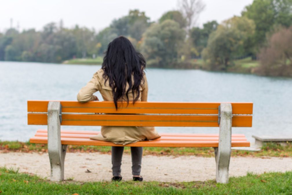 Frau sitzt auf einer Bank und blickt auf einen See