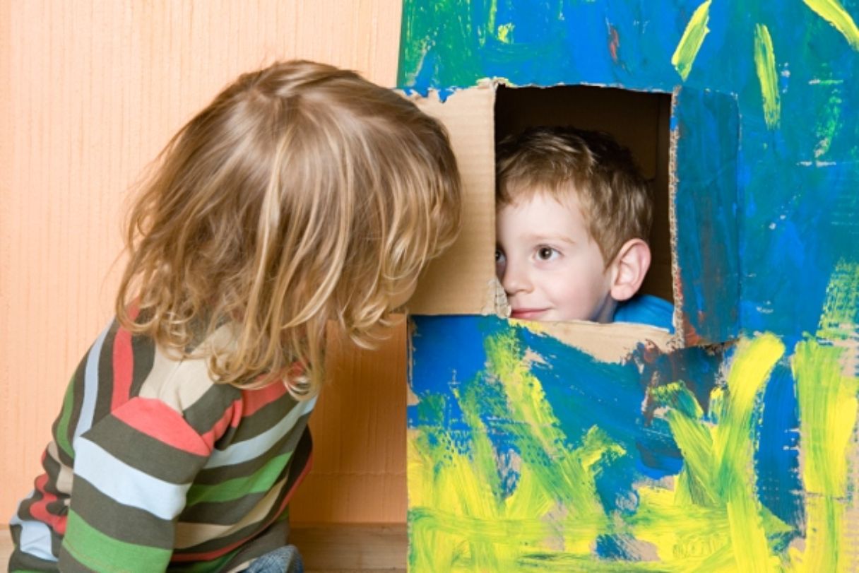 Kind blickt aus dem Fenster eines bemalten Kartons zu einem anderen Kind 