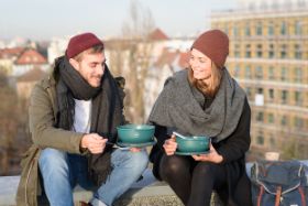 Junger Mann und junge Frau sitzen auf Dachterrasse und essen aus den Rebowl-Mehrwegschüsseln 