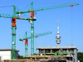 Baustelle mit drei Kränen in München. Im Hintergrund ist der Fernsehturm zu sehen.