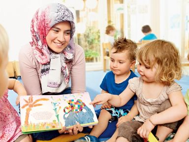 Muslimische Erzieherin mit Kopftuch zeigt Kindergartenkindern ein Bilderbuch