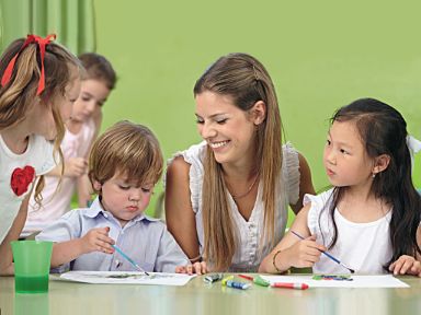 Eine Tagesbetreuungsperson sitzt mit Kindern um einen Tisch. Die Kinder malen mit Wasserfarben.
