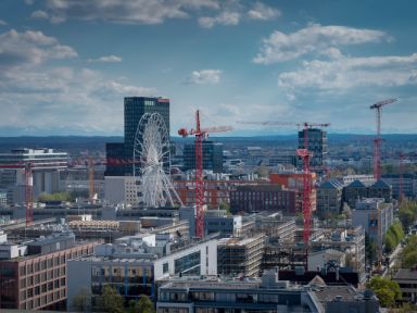 Blick auf das Münchner Werksviertel mit einigen Gebäuden noch im Bau und im Hintergrund die Bergkette bei Fön