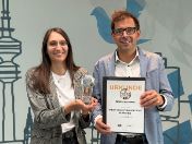Zwei Personen (oder die Namen der Personen) halten eine Glastrophäe und eine Urkunde für die Auszeichnung „TOP ABH 2026“ in der Kategorie Digitalisierung des Kreisverwaltungsreferats München in die Kamera.