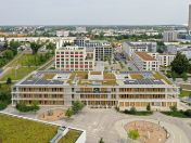 auf dem Bild ist das Gebäude der Grundschule Bauhausplatz von oben zu sehen. Im Hintergrund sieht man München. Es befinden sich keine Menschen auf dem Schulhof.