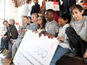 Auf dem Bild sind Schüler*innen auf einer Bühne zu sehen, die den Münchner Schulpreis in der Hand halten und lachen. 