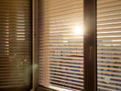Das Bild zeigt den Blick aus einem Fenster in's Freie. Das Fensdter ist mit einer teilweise geschlossenen Jalouisie verdeckt, die die Sonne abschirmt.