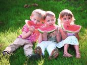 Drei Kinder sitzen im Gras und essen Wassermelone